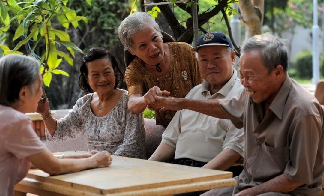 A group of elderly friends sharing laughter in a garden setting - capturing the joy, dignity, and social connection that define elderly care in the Mekong Delta