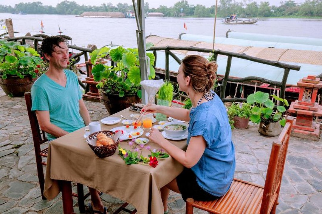 Guests enjoying breakfast or a meal by the riverside view at Mekong Lodge — a moment often praised for tranquility, views and food in guest feedback