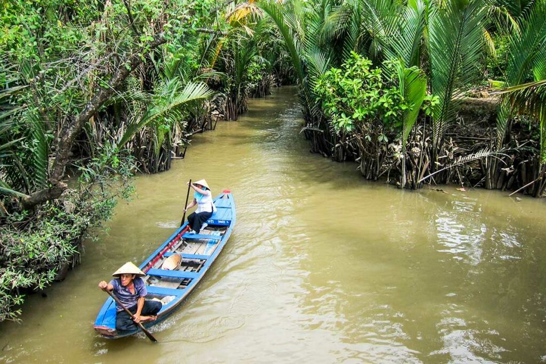 Small boat gliding through narrow canal under canopy of water coconut palms — quintessential riverside scenery in Ben Tre