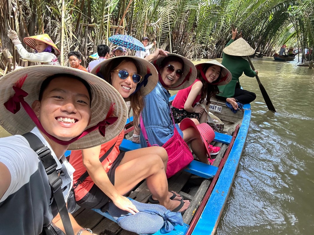 Smiling tourists cruising down narrow coconut-lined waterways during an organized tour in Ben Tre