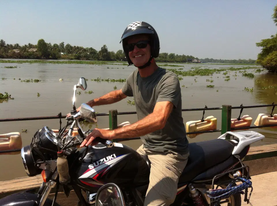 Solo rider navigating riverside terrain with lush foliage — ideal for experienced motorbike touring between HCMC and My Tho