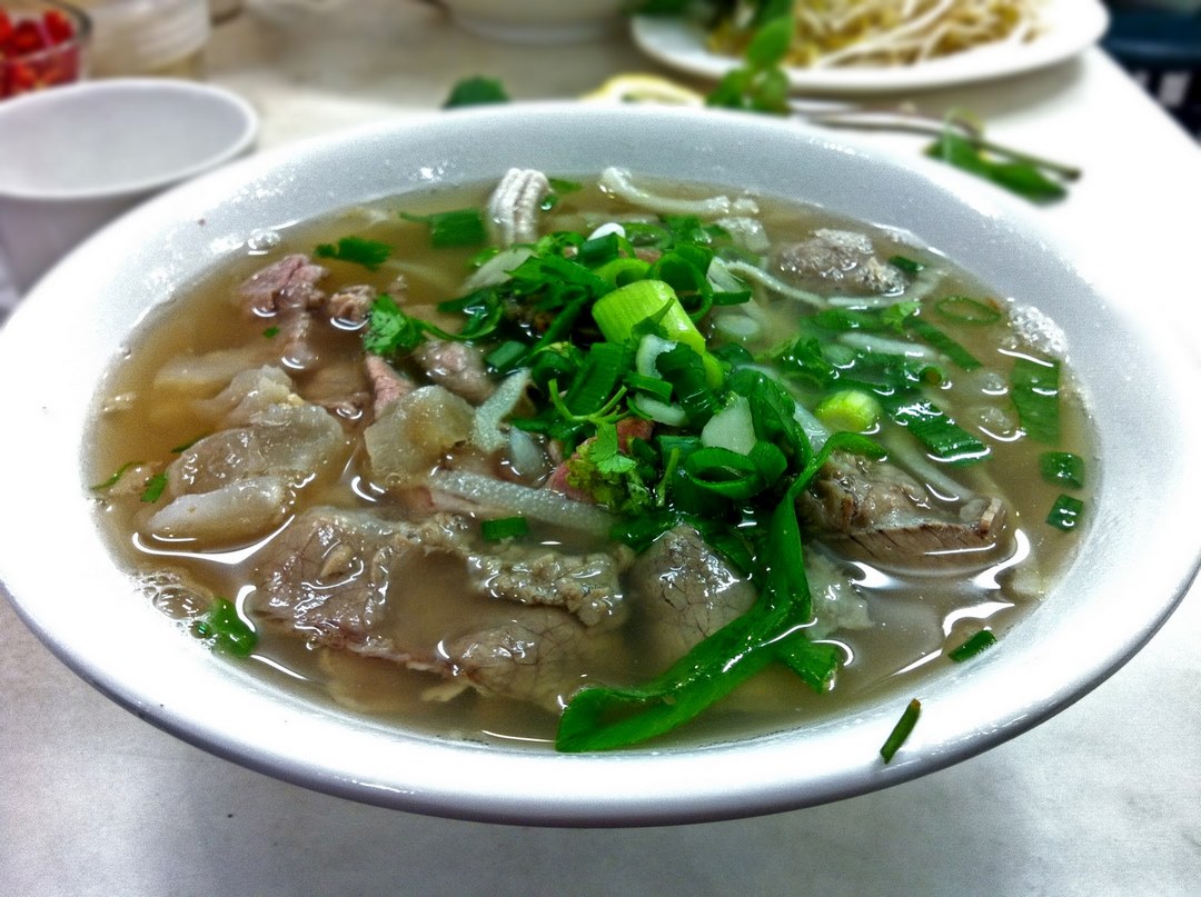 Steaming bowl of beef phở topped with fresh herbs and scallions