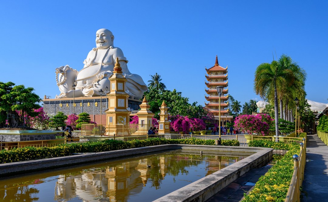 The stately white Budai statue and ornate pagoda reflected in the pond at Vinh Trang Pagoda — a centerpiece of My Tho’s cultural landscape