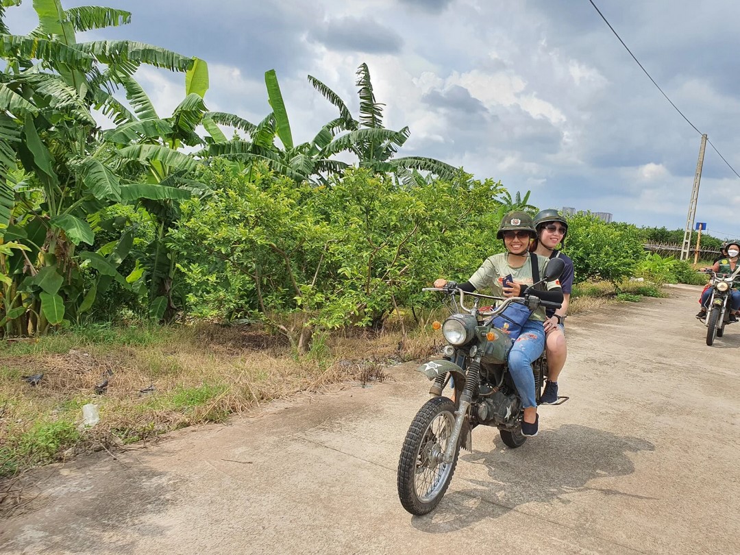 Two people riding a classic motorbike along a tree-lined path — showcasing the kind of freedom motorbike journeys offer