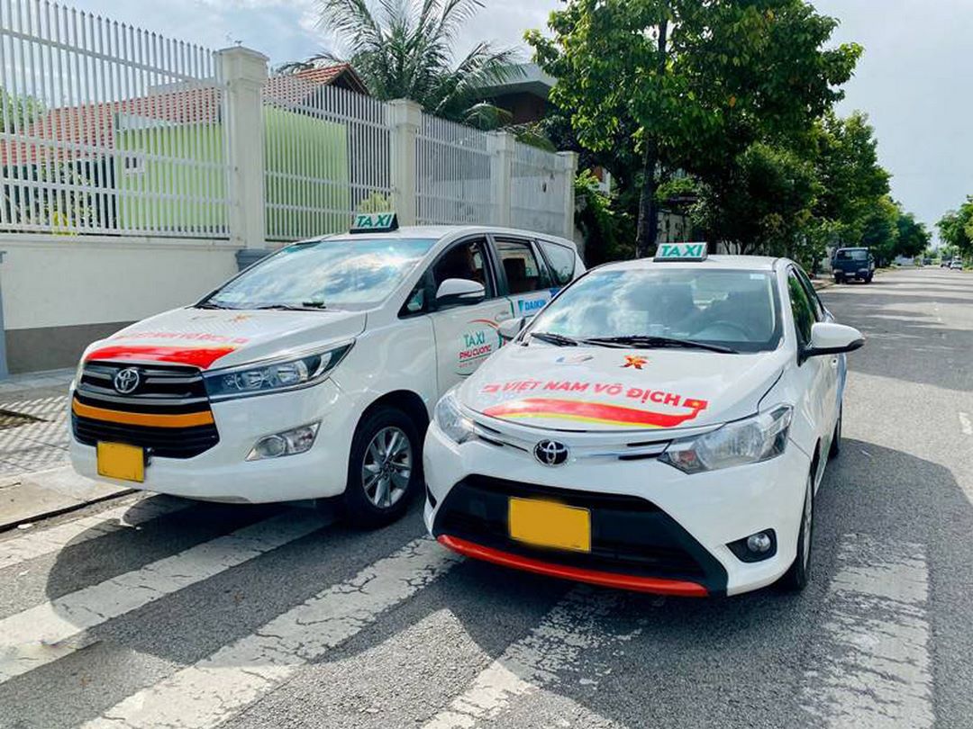 Two white taxis lined up on a street corner in My Tho - shows local taxi private car infrastructure