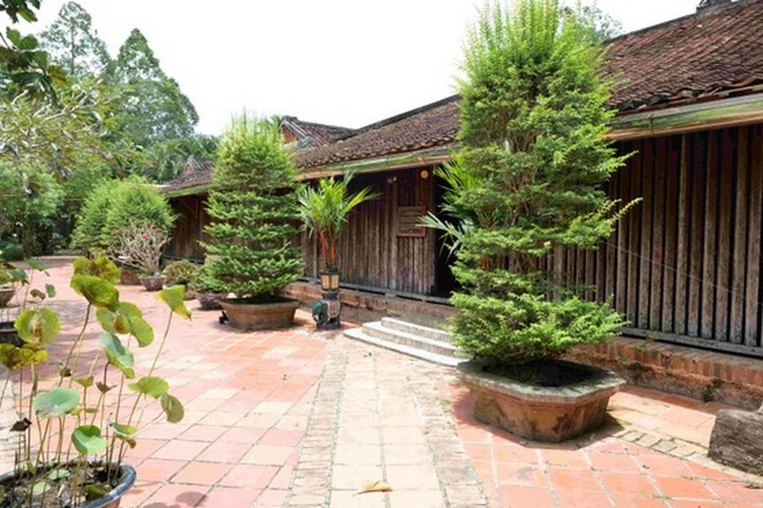 Front view of Phu Hiep Ancient House with traditional red tiled roof and wooden walls, surrounded by lush plants
