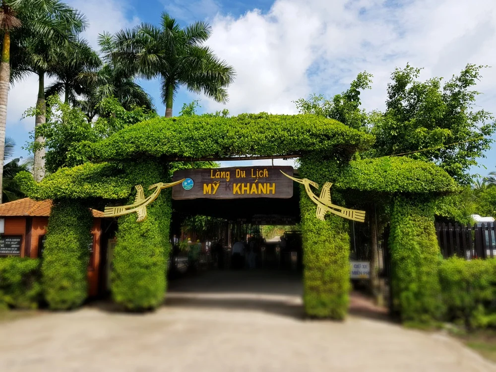 The lush entrance archway of My Khanh Tourist Village with traditional tropical surroundings.